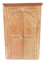 A Georgian pine corner cupboard, the outswept pediment over a pair of arched panelled doors, opening