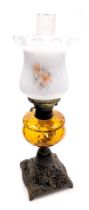 An early 20thC oil lamp, with an opaque shade decorated with flowers, an amber glass central reservo