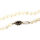 A string of uniform cultured pearls, on a 9ct gold and garnet three stone clasp, 46cm long.