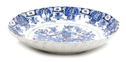 An 18thC Delft blue and white charger, with a wavy border, the centre decorated with a vase surround