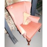 A pink upholstered wing back armchair, raised on shell capped supports. This lot is located at our a