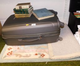 A wheelie suitcase, group of books and a small machine made rug.