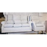 A sofa suite, comprising a three seater cream sofa and armchair with scroll decoration.