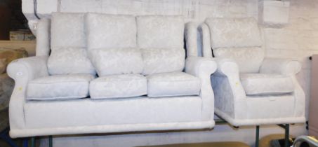 A sofa suite, comprising a three seater cream sofa and armchair with scroll decoration.