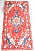 A small red ground rug, with central geometric patterns and borders. (Dimensions 140cm x 70cm).This