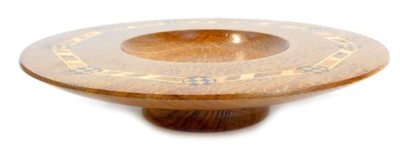 A 20thC oak and inlaid footed bowl, with a shallow recess to centre surrounded by a wide border with