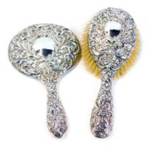 A George V silver backed hand mirror and matching brush, both with repousse decorated designs of mas