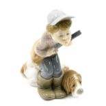 A Lladro porcelain figure group modelled as a young boy crouching holding gun beside hound, printed