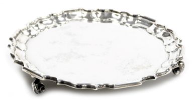 An Edward VII circular silver card tray, with piecrust border, raised on three stylized leaf capped