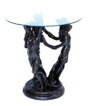 A glass top occasional table, raised on three bronzed plaster figures of ladies standing upon a rug,