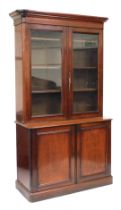 A Victorian mahogany cupboard bookcase, the outswept pediment above a pair of glazed doors enclosing