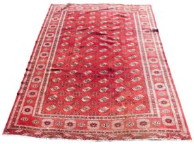 A Bokhara red ground rug, the central rectangular field decorated with repeating floral medallions,