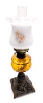 An early 20thC oil lamp, with an opaque shade, decorated with flowers, an amber glass central reserv