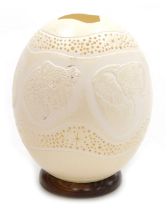 An ostrich egg night light, carved with wild animals, within pierced star and dot borders, on a turn