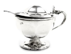 A George V silver mustard pot, of circular footed form, with a hinged lid, blue glass liner and spoo