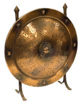 A late 19thC copper fire screen, of circular embossed shield form, raised on cast iron supports, 57c