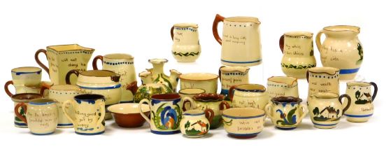 A group of early 20thC Devon Motto Ware pottery, including cream jugs, a shaving tyg and loving cup.