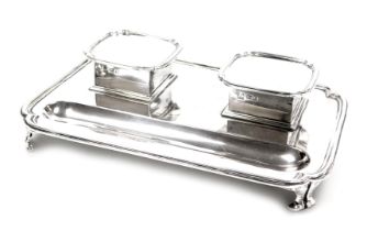 A George V silver desk stand, with a pair of hinged lidded glass inkwells, and pen recess, raised on