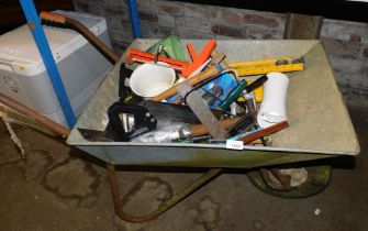 A galvanised wheelbarrow containing a quantity of hand tools.