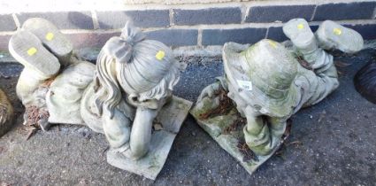 Two garden ornaments in the form of two children reading books.
