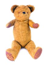 An early 20thC plush blonde jointed straw filled Teddy bear, with amber glass eyes, and pad paws and