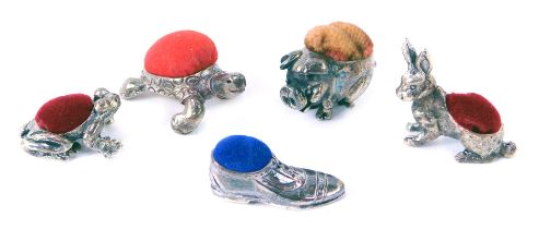A group of white metal miniature pin cushions, modelled as pig, tortoise, hare, frog and shoe, each