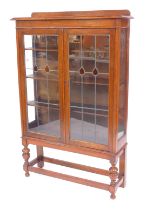 An early 20thC oak display cabinet, the top with a raised back, above two leaded glazed doors enclos