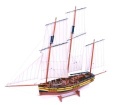 A model of a three masted sailing vessel, wooden hull, fully rigged with sails, on a black and yello
