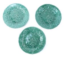 Three green majolica relief moulded plates, decorated with flowers and leaves, 23.5cm diameter.