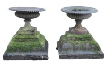 A pair of cast metal garden urns, each of cylindrical form, with lappet border, on a stepped stone b