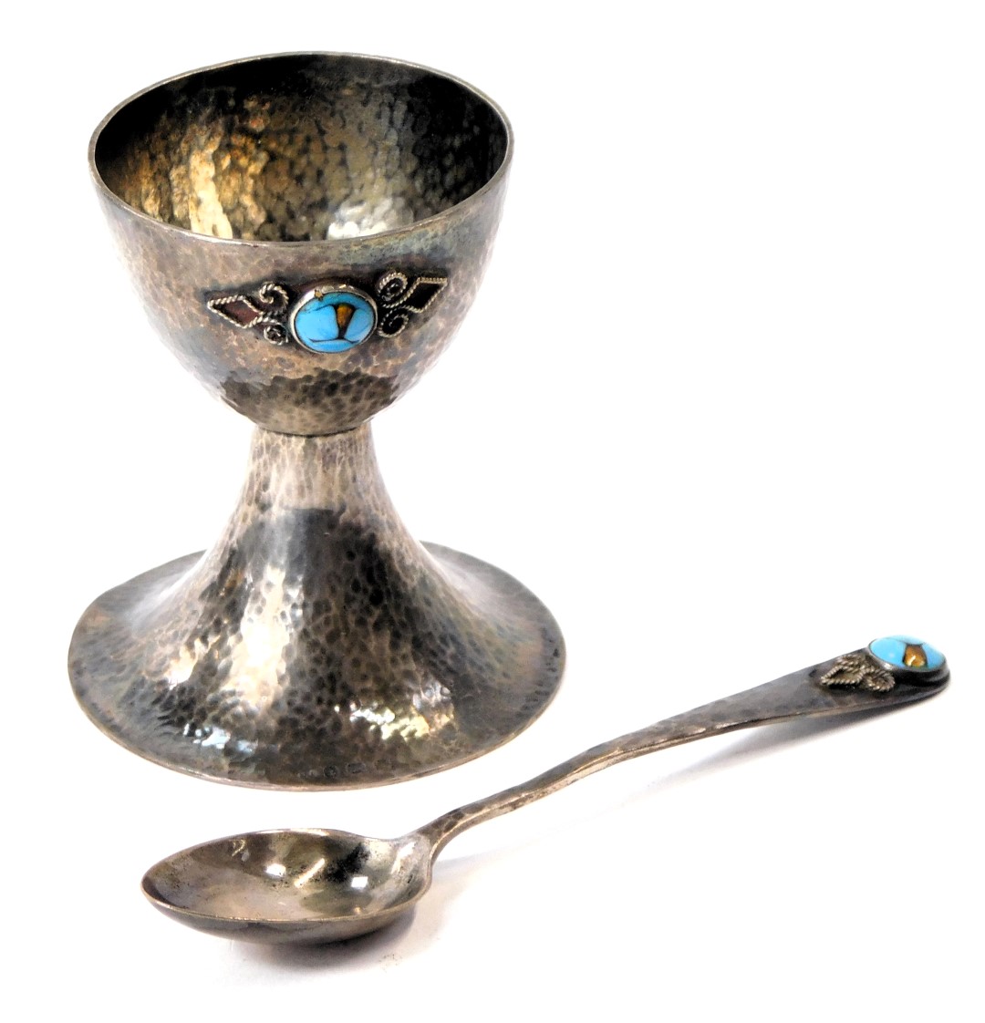 An Arts and Crafts hammered silver egg cup and spoon, the body of hammered design with scroll applie