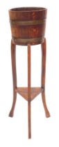 An early 20thC oak plant stand, the circular top with cooper banding, on square outswept legs united