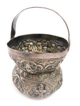 An Eastern white metal basket, with arched and ribbed handle, with embossed decoration of figures, w