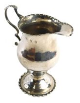 A George IV silver helmet shaped cream jug, with beaded borders, a domed foot and a scroll handle wi