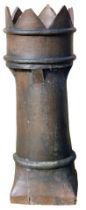 A reconstituted stone chimney pot, with a six sectional crenilated top, on a cylindrical body and sq