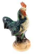 A pottery figure of a cockerel, overpainted with blue, green, and brown, 25.5cm high.