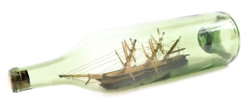 An early 20thC glass ship in a bottle, of cane three mast structure, on rocky supports with cork sto