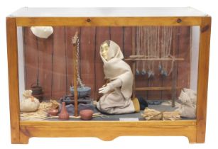A diorama model of a Saxon peasant woman, with spinning loom, cooking bowl, etc., in a Perspex glaze
