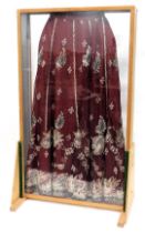 A red silk skirt, embroidered with design of peacocks, in metallic thread, mounted into a floor stan