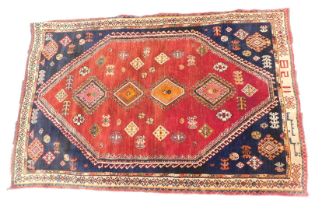 A Persian rug, with a design of multi coloured pole medallion on a red ground with blue spandrels, o