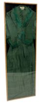 A Victorian green pattern silk full length dress, with tassel borders, in perspex and wooden case, t