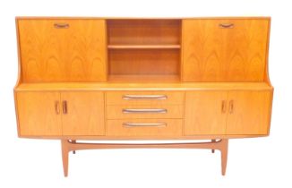 A 1970's teak sideboard, the raised top with a two fall-front doors, flanking a shelf the base with