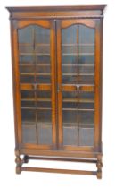 An early 20thC oak bookcase, with a moulded cornice above two full length glazed doors, on cup and c