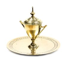 A Victorian brass inkwell, of trophy form, with a ceramic inset, raised on a circular base, 16.5cm w