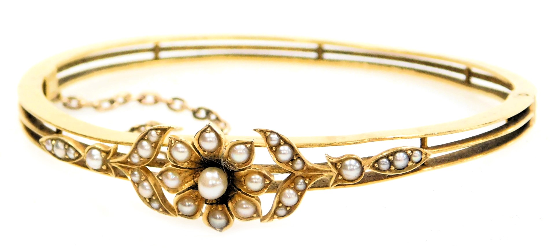 An Edwardian 15ct gold and seed pearl bangle, in a floral and open work design, on a snap clasp, wit