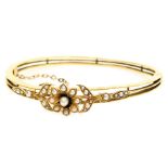 An Edwardian 15ct gold and seed pearl bangle, in a floral and open work design, on a snap clasp, wit