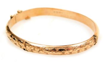 A 9ct rose gold hollow bangle, foliate engraved on a snap clasp, with safety chain as fitted, 6.4g.