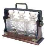 An early 20thC oak and silver plated tantalus, with three cut glass decanters and stoppers, 34.5cm w