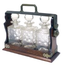 An early 20thC oak and silver plated tantalus, with three cut glass decanters and stoppers, 34.5cm w