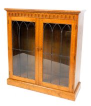 An Old Charm type oak bookcase, with a pair of glazed doors, enclosing two shelves, raised on a plin